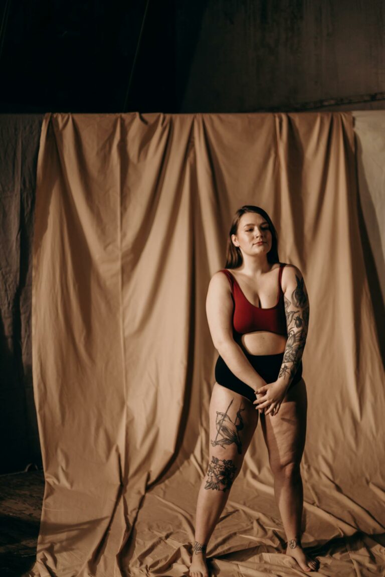 A tattooed woman confidently poses indoors, showcasing her body art.